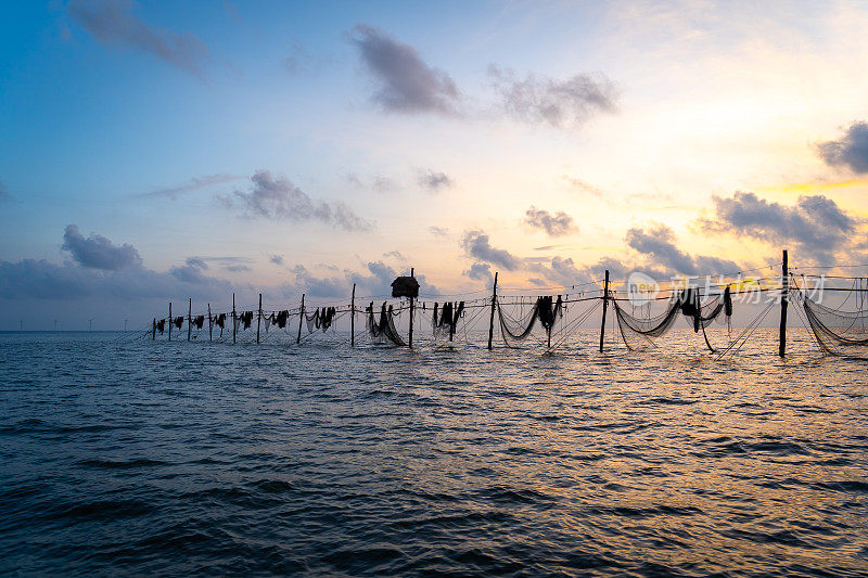 在日出期间，越南Tra Vinh省的渔民在海上拉鱼竿上的渔网的剪影，当地人称之为Day hang khoi。